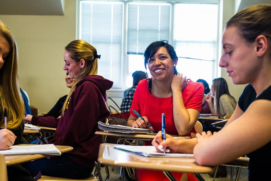 Four female students sit at desks in a classroom writing notes for their psychology class.