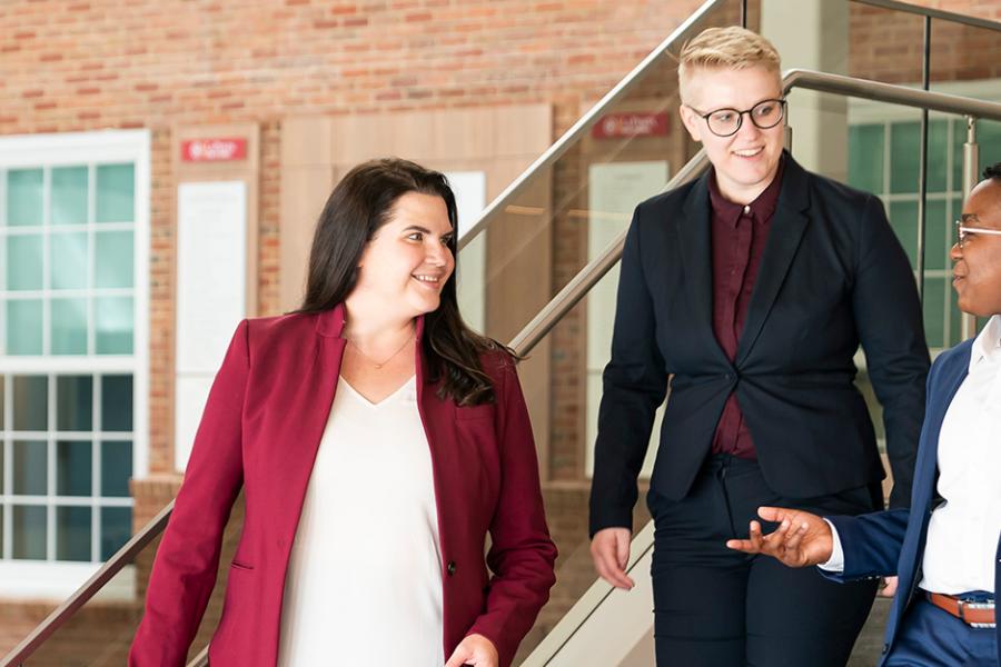 Three graduate students walk down the stairs in the LaPenta School of Business.