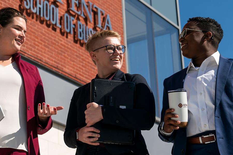 Three graduate business students walk in front of the LaPenta School of Business building on a sunny day.
