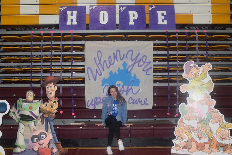 A member of Colleges Against Cancer sits under a sign that says hope and a banner that says when you wish upon a cure.