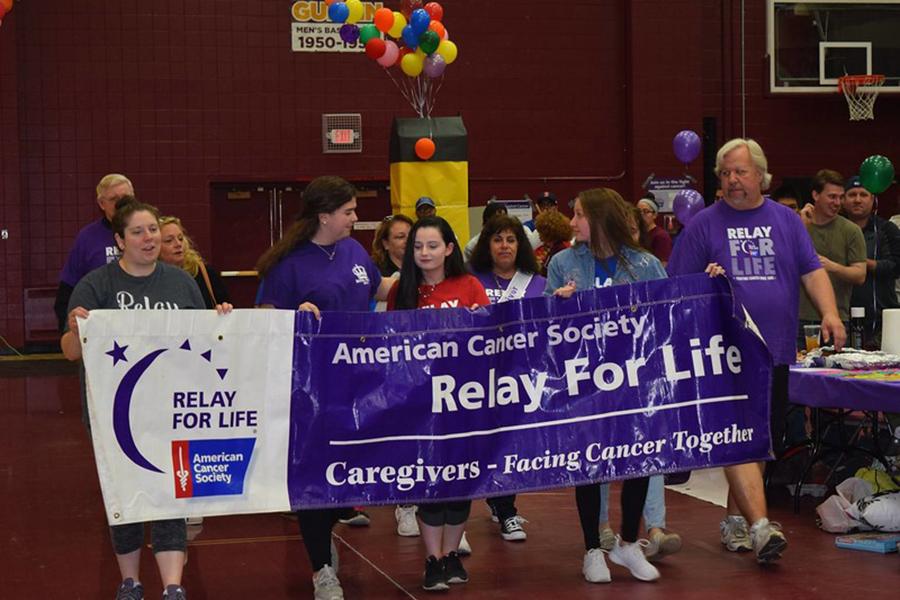Members of Colleges Against Cancer hold a Relay for Life banner in the gym.