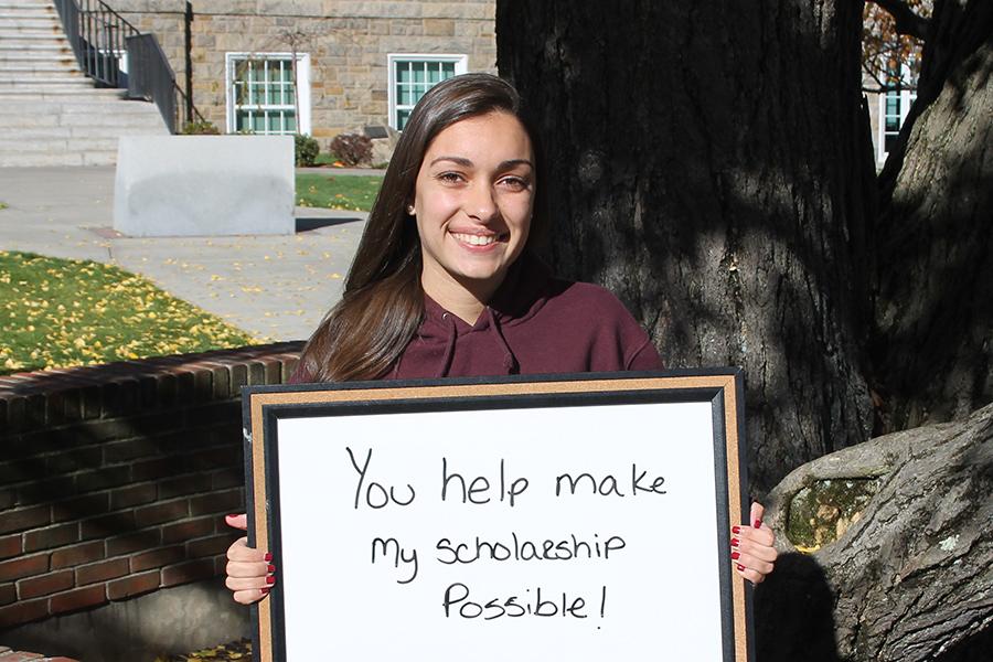 A student smiles and holds a sign that says You help make my scholarship possible.