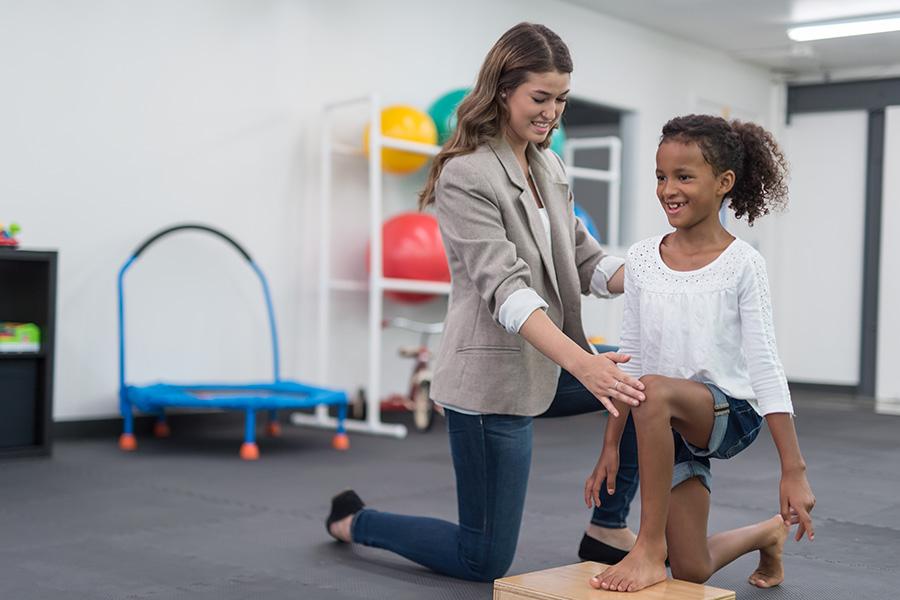 A female occupational therapist assists a young female child in a session.