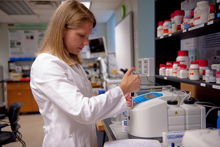 A female student in a white lab coat works on a chemistry experiment.