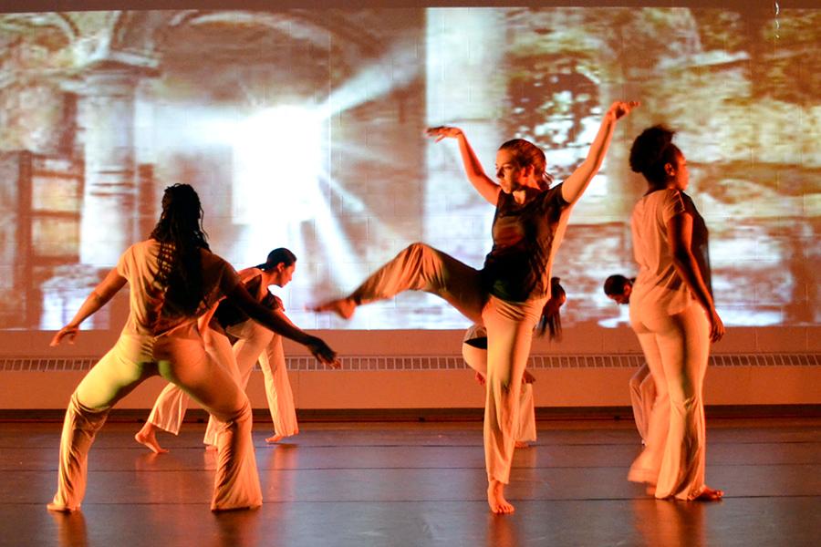 A dance ensemble performs with a video screening in the background.