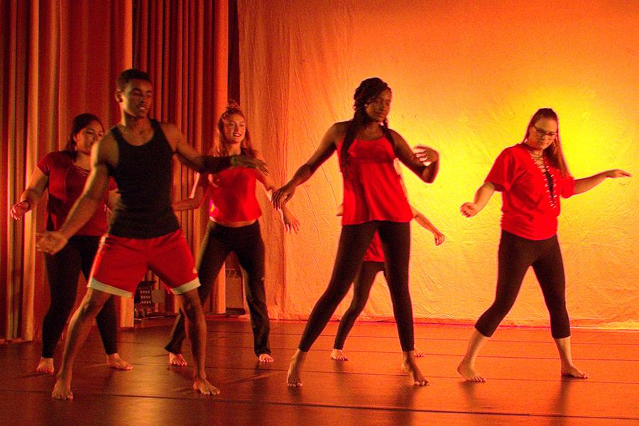 A group of students perform in a dance ensemble with orange lighting.