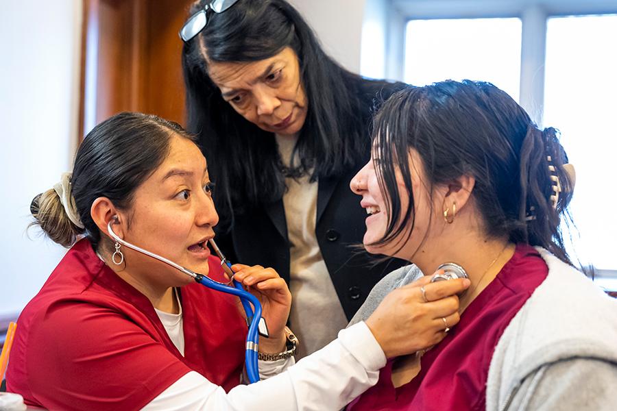 Two speech-language pathology students practice with a stethoscope while the professor watches..