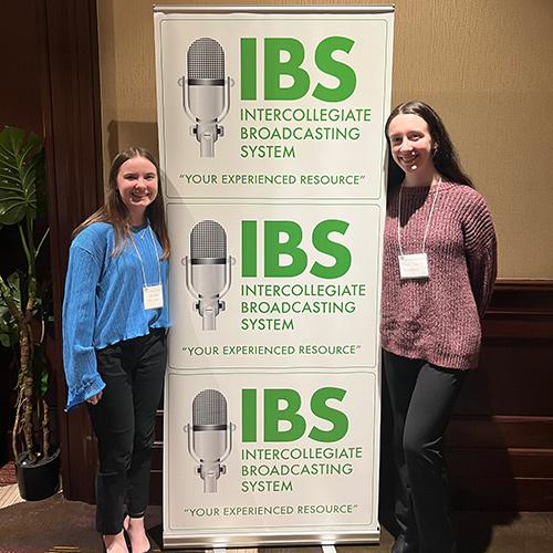 Two Iona students pose with the IBS banner.