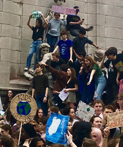 Demonstrators in support of climate change climb up on a statue and hold up posters.