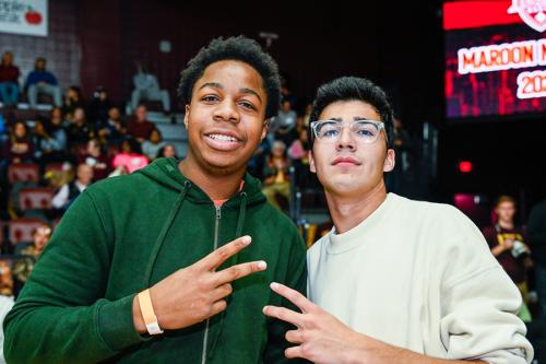 Two friends smile and give the peace sign at a basketball game.
