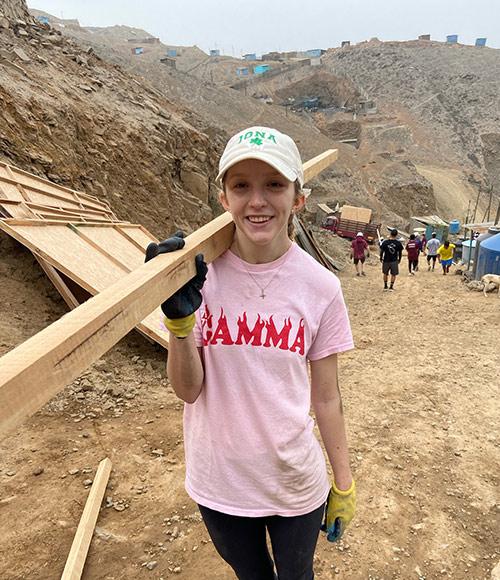 A student carries a board up the mountain in Peru to build a house.