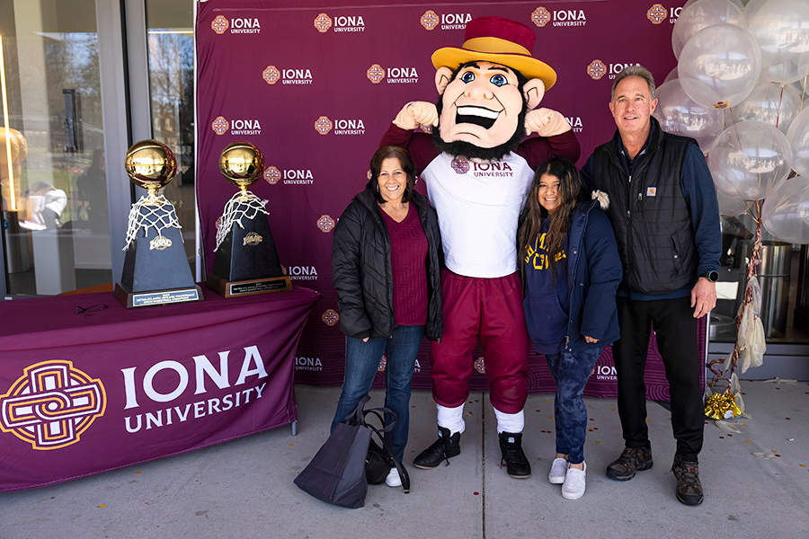 Killian poses with a family in front of some MAAC trophies.