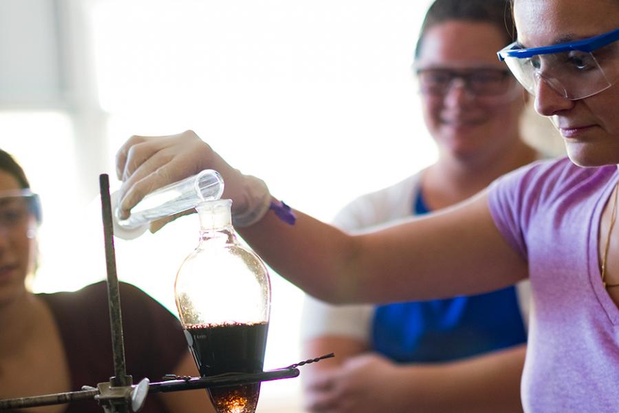 Three students are working in a biochemistry lab while wearing goggles.