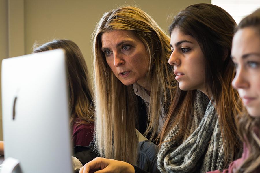 A professor helps a student working on a computer.