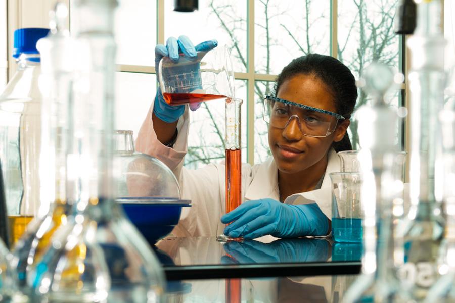 A chemistry student pours liquid from a beaker into a graduated cylinder.