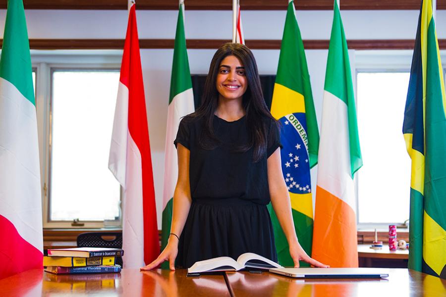 An international business student stands in front of a row of flags from several different countries.