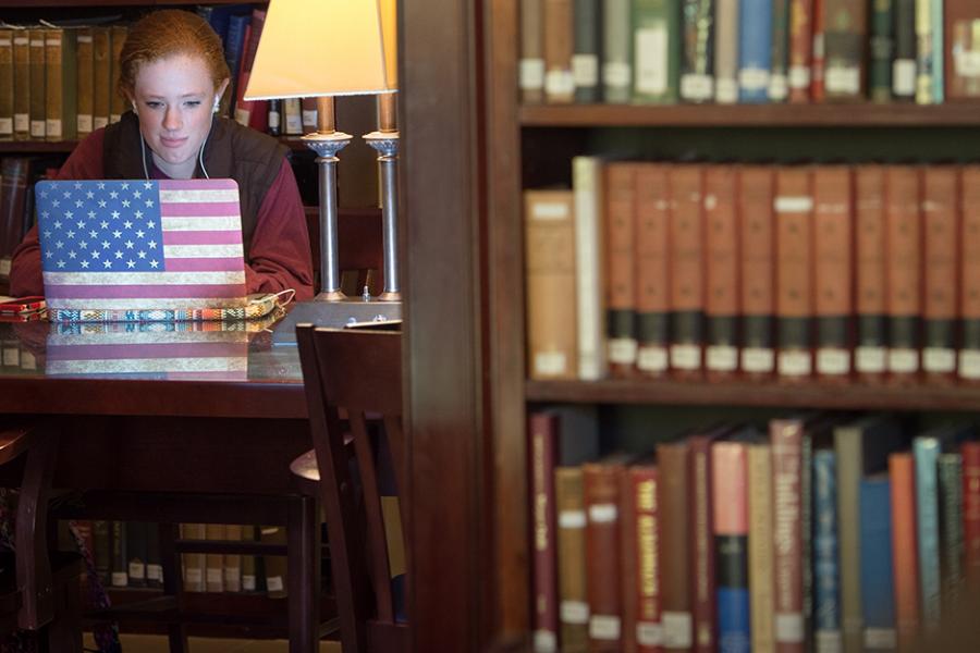 A student works alone in the library. Her laptop has an American flag overlay.