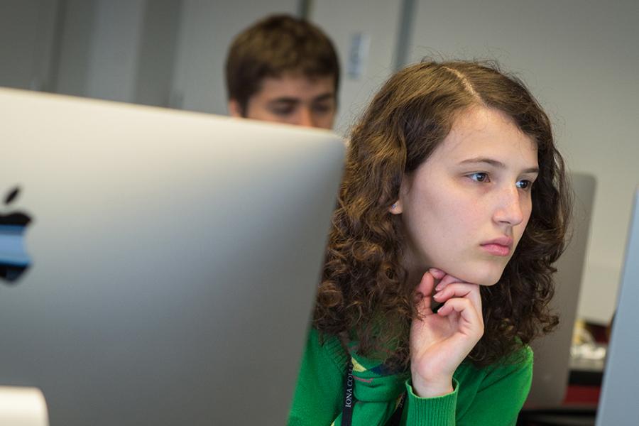 A student sits between two iMacs and works in the computer lab.