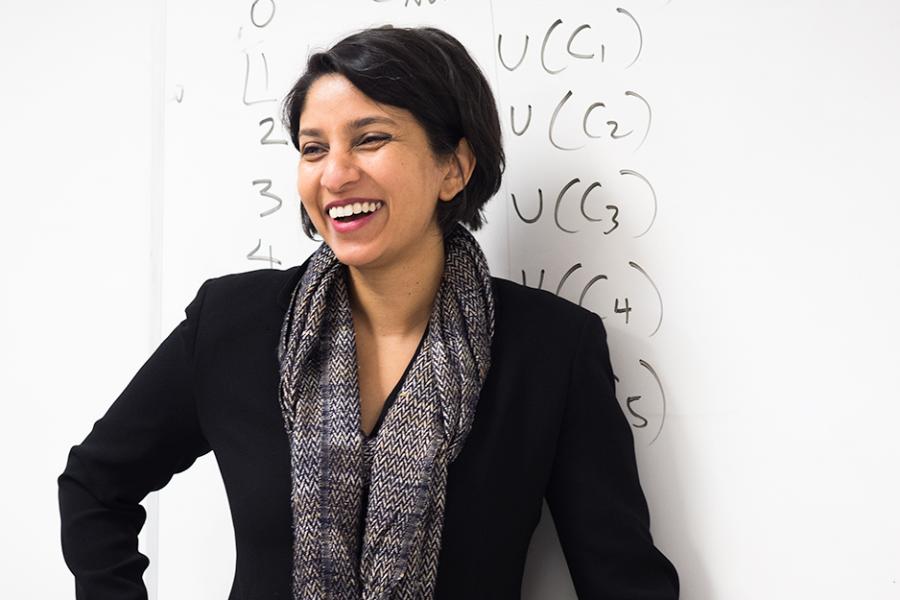 A professor stands in front of the white board and smiles.