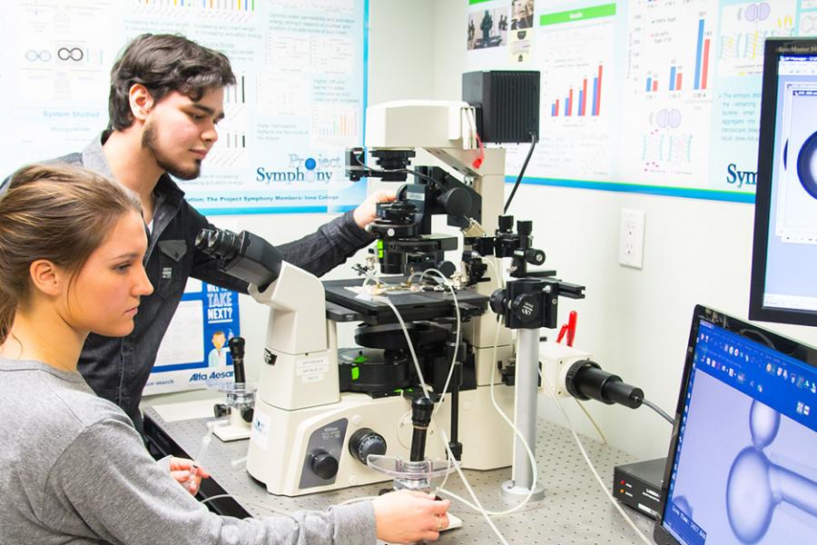 A male student and female student use chemistry equipment while looking over a computer monitor