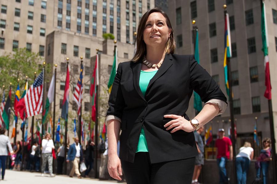 A student visits Rockafeller center in New York City and stands near the flags of the world.