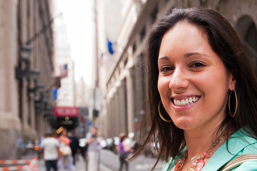 A student in a green jacket smiles toward the camera in New York City.