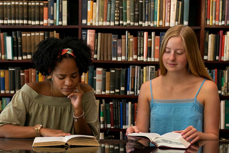 Two students sit in the library to read books for a history class.