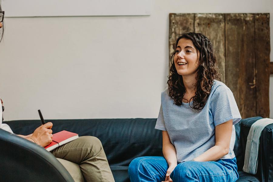 A therapist sits on a chair and talks to her patient on a couch.