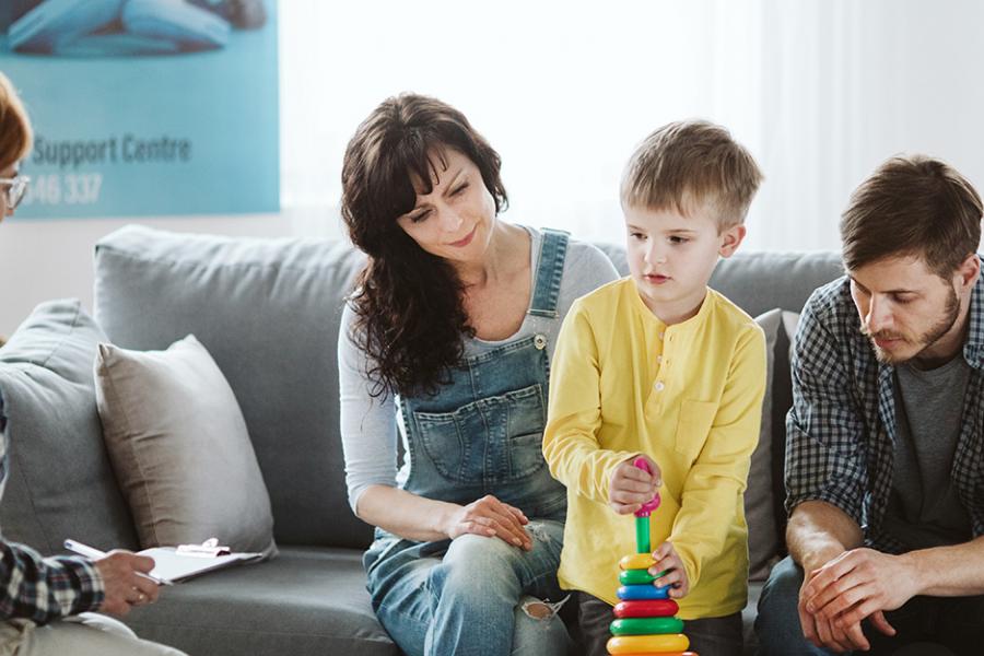 A mother, father and young male child sit on a couch at a therapy session with a female therapist