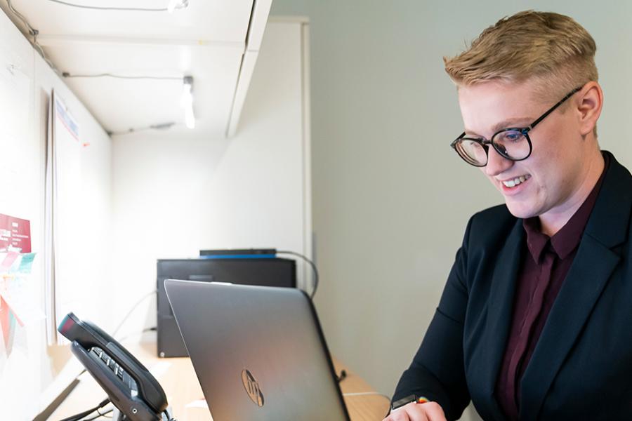 A student in black suit and maroon shirt works on their Online MBA on a laptop in their office.