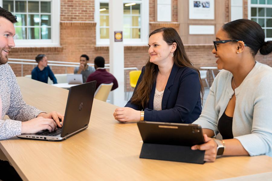 Three students work on laptops in the atrium in LaPenta School of Business.