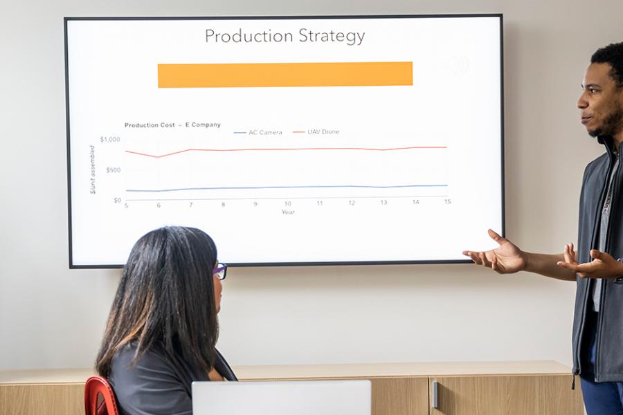 Students work in a conference room in the LePenta School of Business and their Production Strategy is projected on a screen. 
