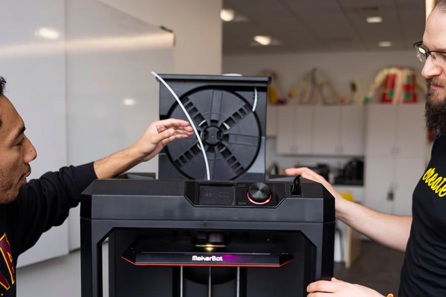 A student and a teacher work with the Makerbot at the Hynes Institute.