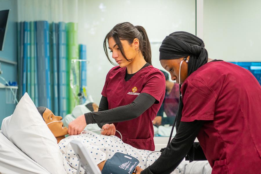 Two Iona nursing students practice reading vitals on a mannequin.