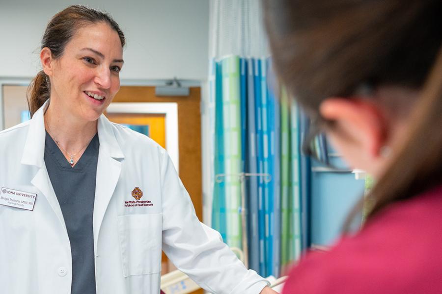 A nursing professor in a white lab coat smiles and helps a student.