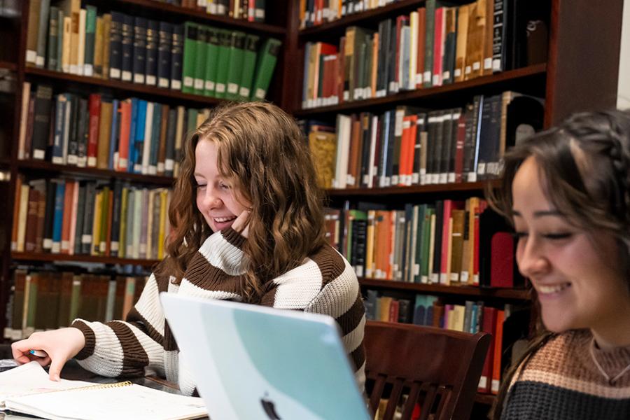 Two students study in the Ryan Library and smile.