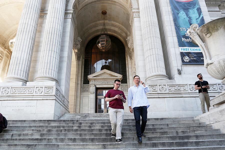 Two students walk down the steps of the NYC public library.