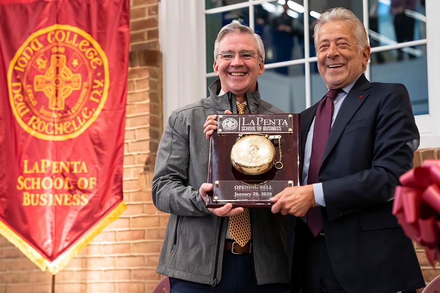 President Carey and Mr. LaPenta hold up the LaPenta opening bell at the ribbon cutting.