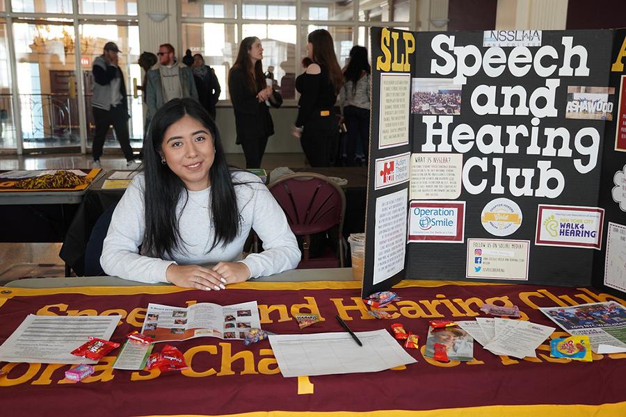 A member of the Speech and Hearing club recruits new members at a table in the LaPenta Student Union.