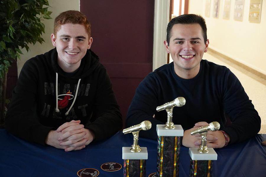 Two club members sit at a table with awards WICR has won.