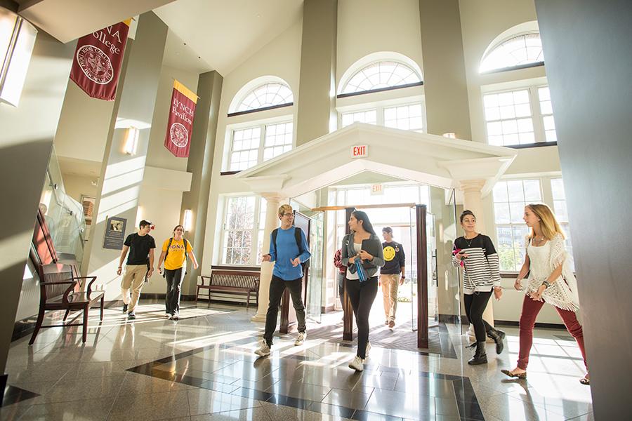 Students enter Ryan Library as beautiful sunlight shines through the glass doors and windows.