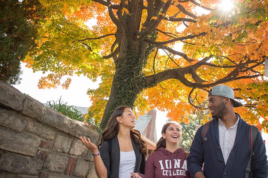 Three students walk in front of campus on a sunny fall day.