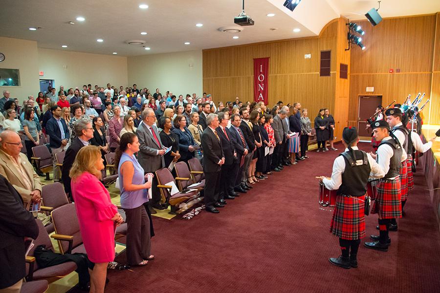 Faculty, staff and students gather at an event in the auditorium while the pipers play.