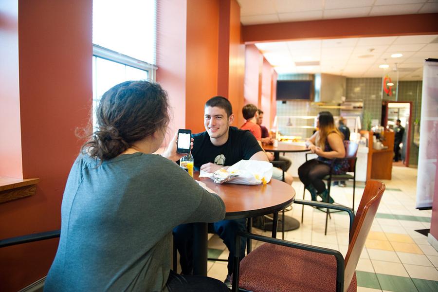 Two students talk at a table while eating lunch in the LaPenta Marketplace.