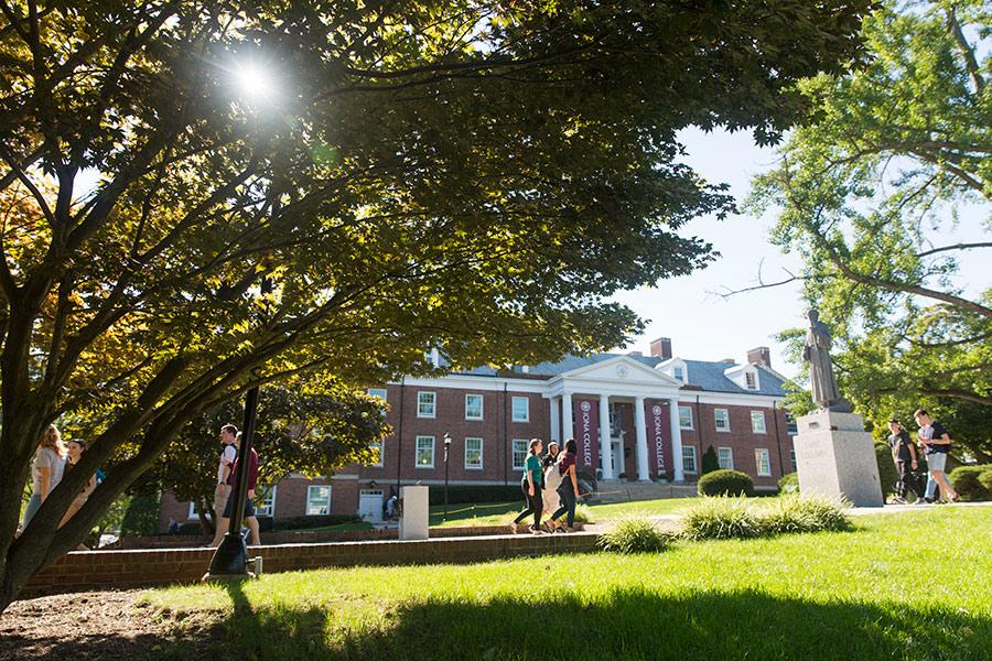 Students walk in front of McSpedon as sunlight shines through the trees.