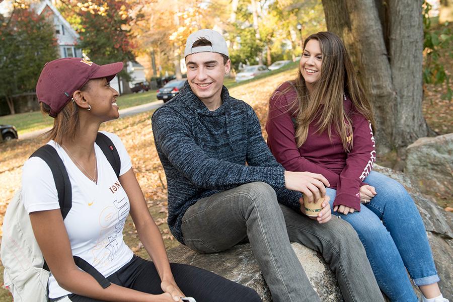 Three Iona students sit outside on a fall day near campus.