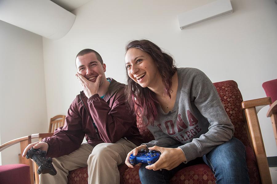 Two Iona students sit on a couch and play video games.