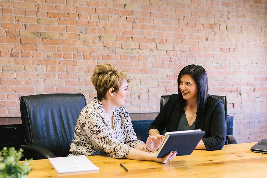 Two women share a conversation while looking at a digital tablet.