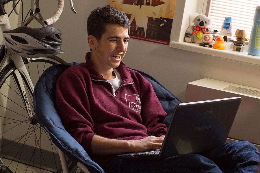 A student in an Iona shirt does a virtual information session on his laptop.