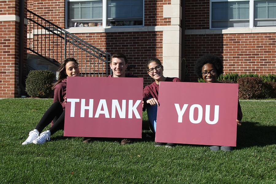 Four students hold two signs saying "Thank" and "You".